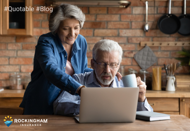 Couple with grey hair working on a laptop in a kitchen.