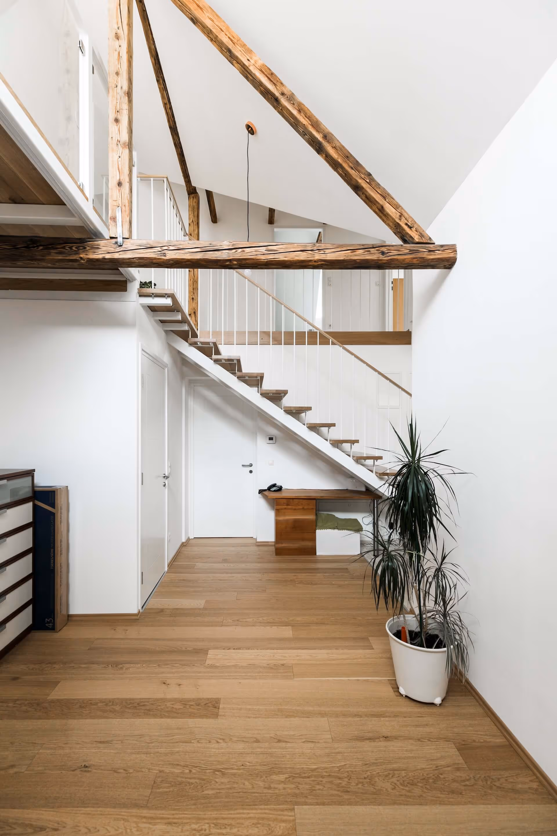 Wohnraum mit sichtbaren Holzbalken, moderner Treppe und Parkettboden.