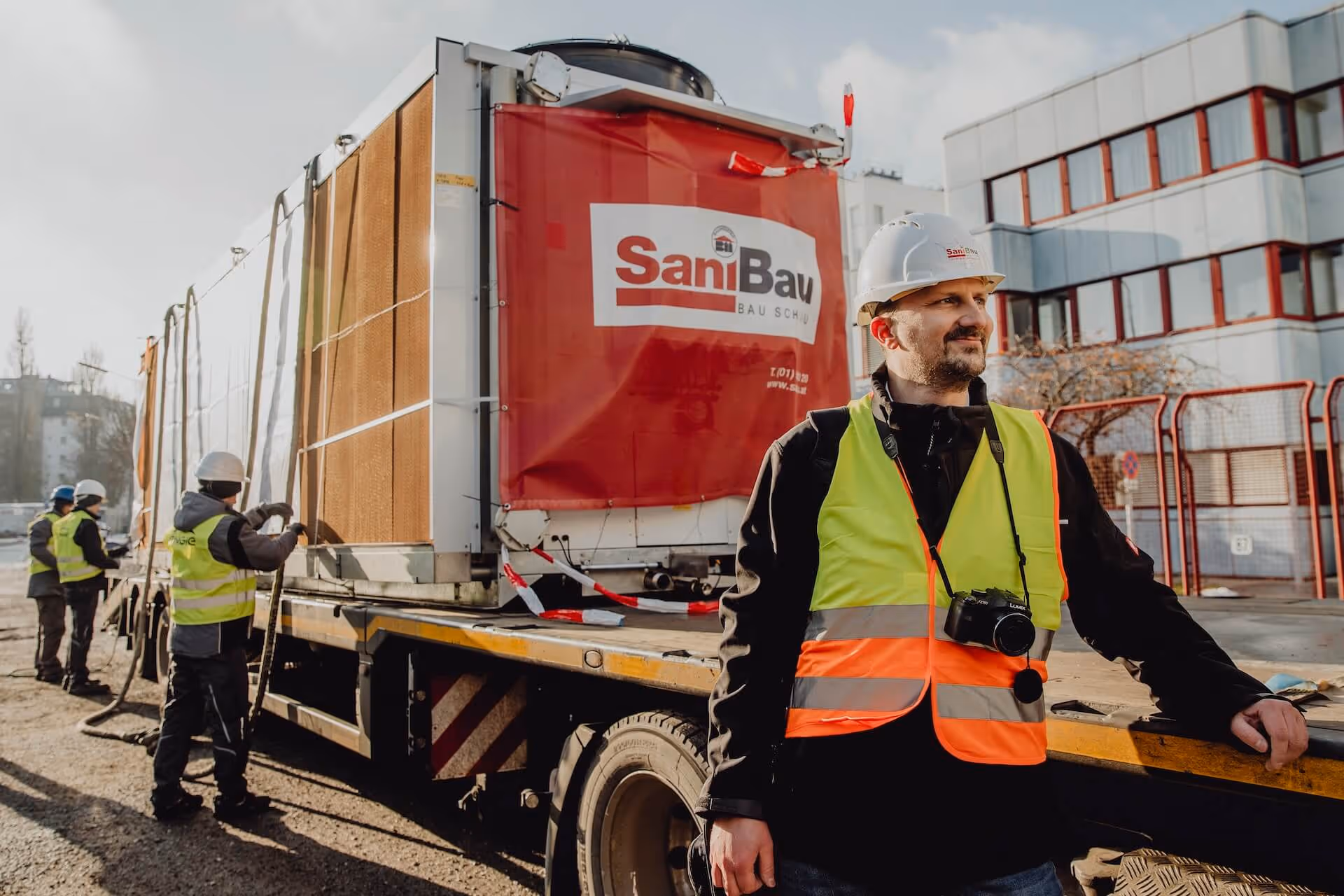 Bauleiter von SaniBau auf Baustelle, während ein Container mit Baugeräten verladen wird