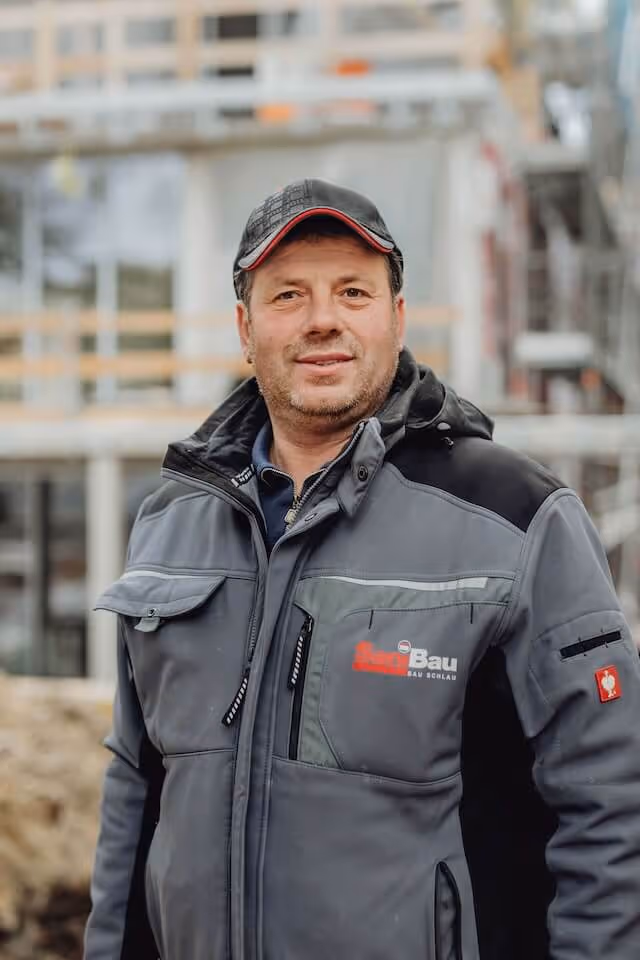 SaniBau Mitarbeiter mit Arbeitsjacke auf Baustelle.