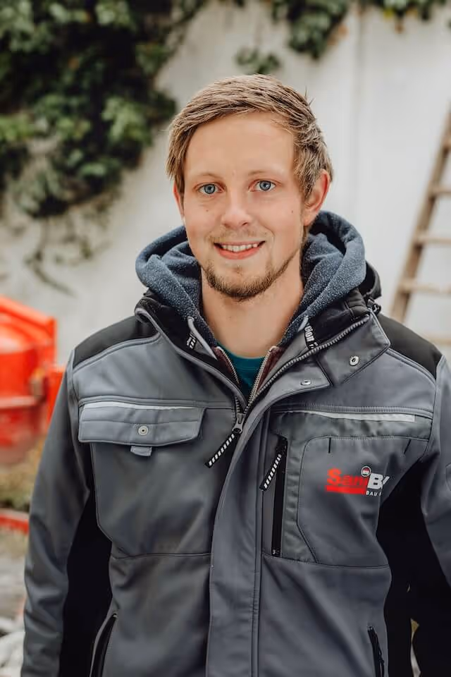 SaniBau Mitarbeiter mit Arbeitsjacke im Außenbereich.