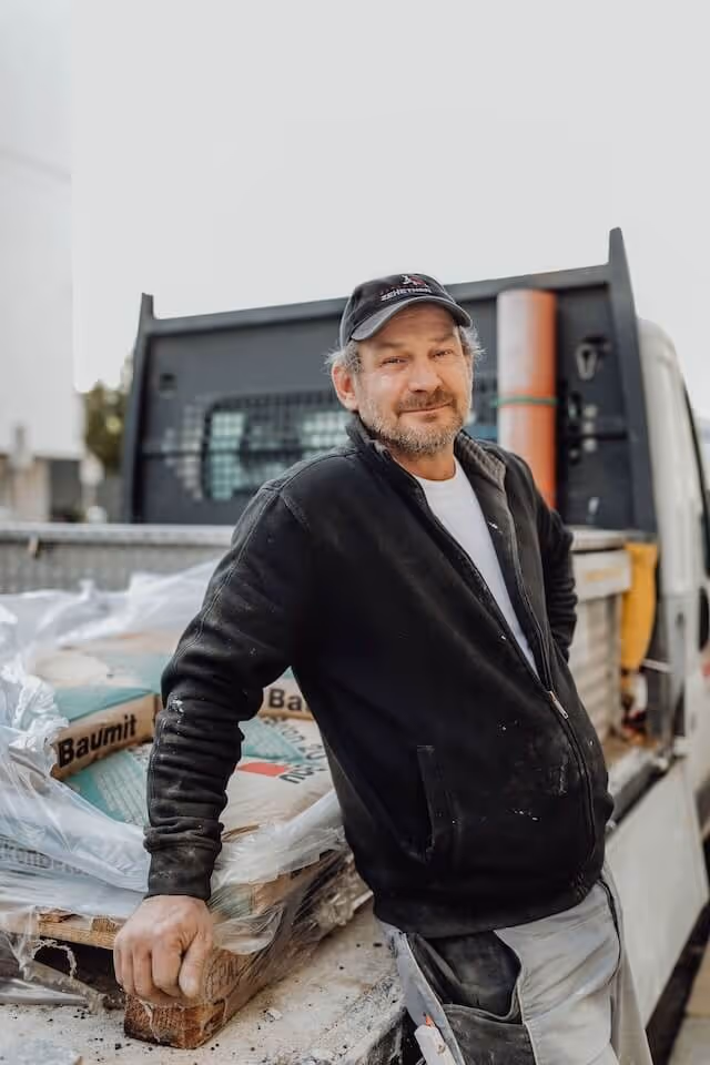 SaniBau Mitarbeiter auf Baustelle lehnt an LKW mit Baumaterial.