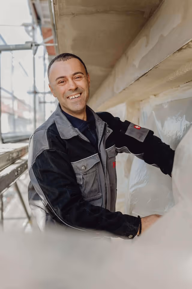 SaniBau Mitarbeiter mit Arbeitsjacke auf Baustelle im Freien.