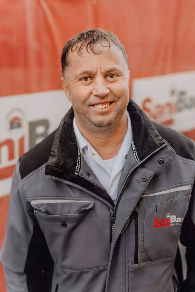 SaniBau Mitarbeiter mit grauer Jacke auf Baustelle.