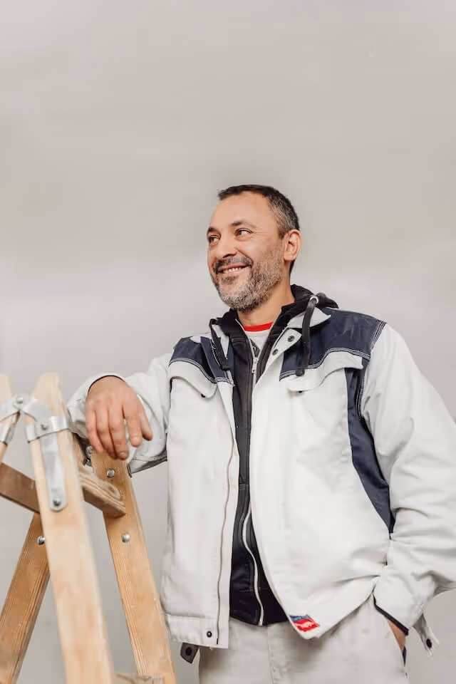 SaniBau Mitarbeiter auf Leiter stehend in Arbeitskleidung auf der Baustelle.