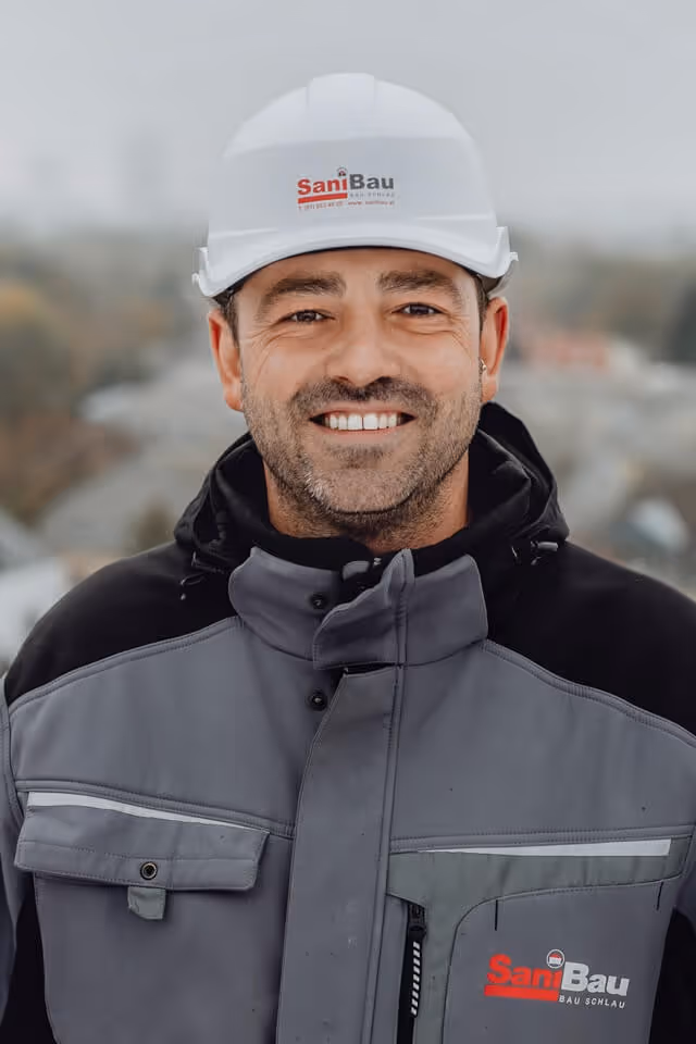 Portrait von SaniBau Mitarbeiter mit SaniBau Jacke und Schutzhelm.