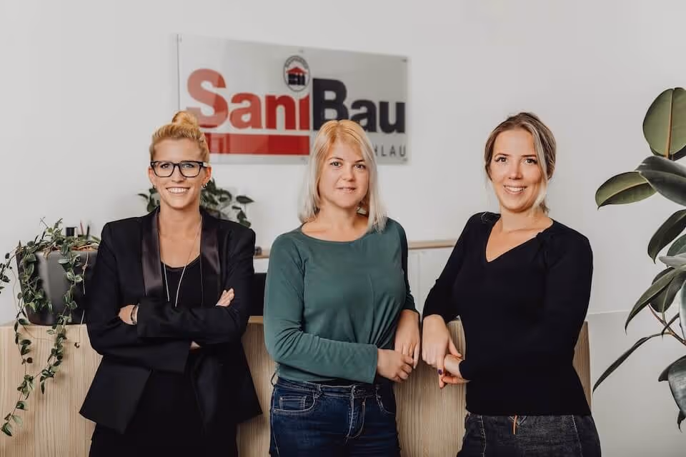 SaniBau Büro-Team vor Unternehmenslogo.