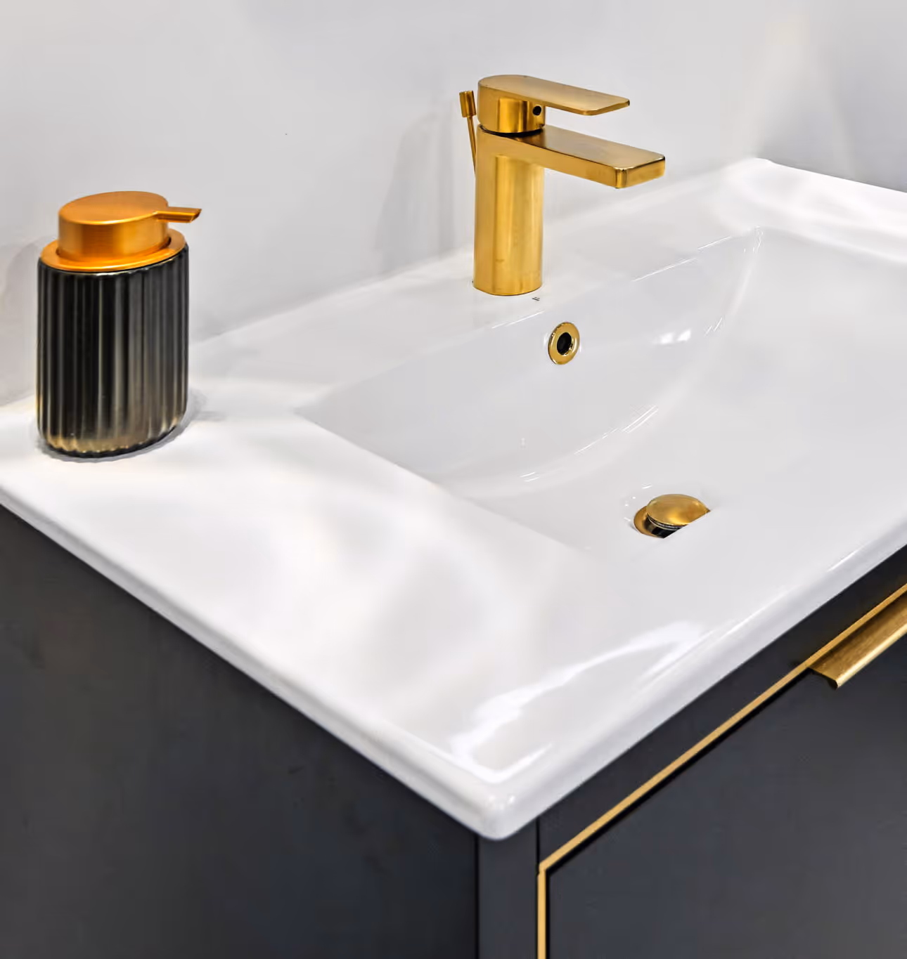 Modern bathroom sink with a gold faucet and matching gold-accented soap dispenser on a black vanity with gold trim.