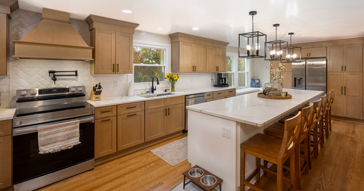 Modern kitchen with wooden cabinets, stainless steel appliances, a large white island with wooden bar stools, and pendant lights.