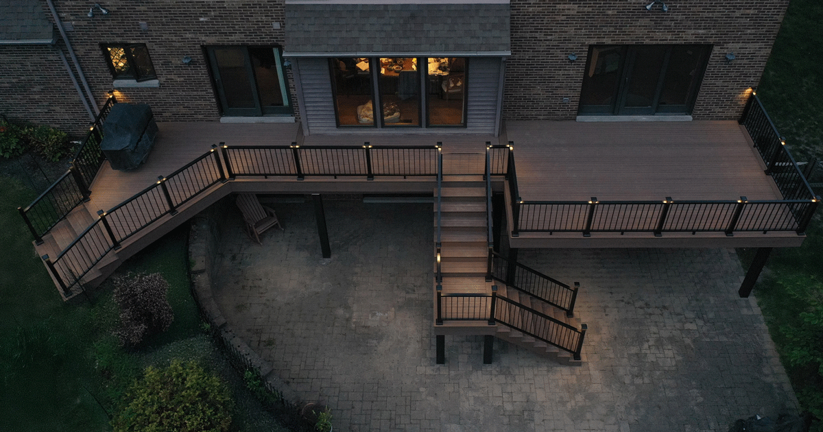 Elevated wooden deck attached to a brick house with black metal railings and built-in lights along the perimeter and steps.