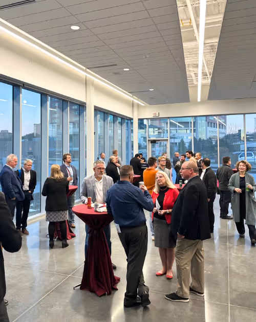 Group of people socializing and networking in a modern indoor space with large windows and high ceilings.