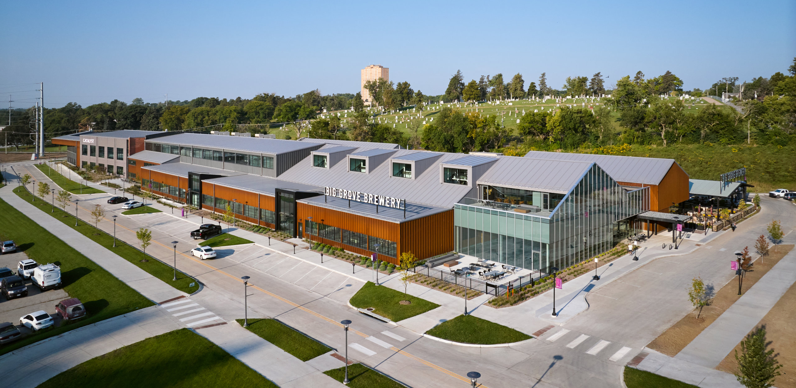 Aerial view of Big Grove Brewery and Catalyst building with surrounding parking and green hills in the background.