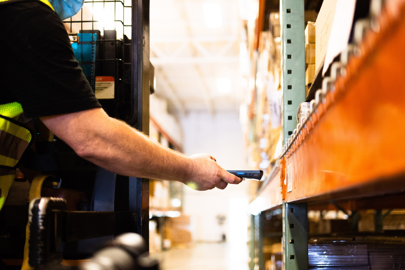 A man is holding a barcode scanner in front of a shelf of items.