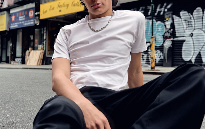A man wearing a white shirt and black pants sits on the street.