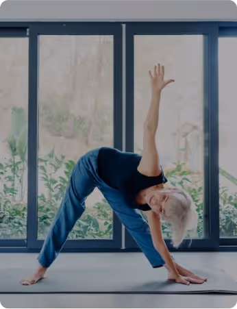 Older woman in blue performing a flexible yoga side bend near window