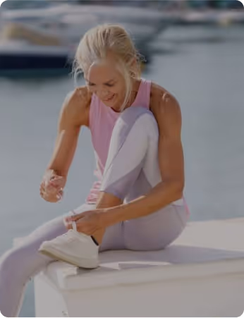 Woman in pink and white athletic wear tying shoe near boats