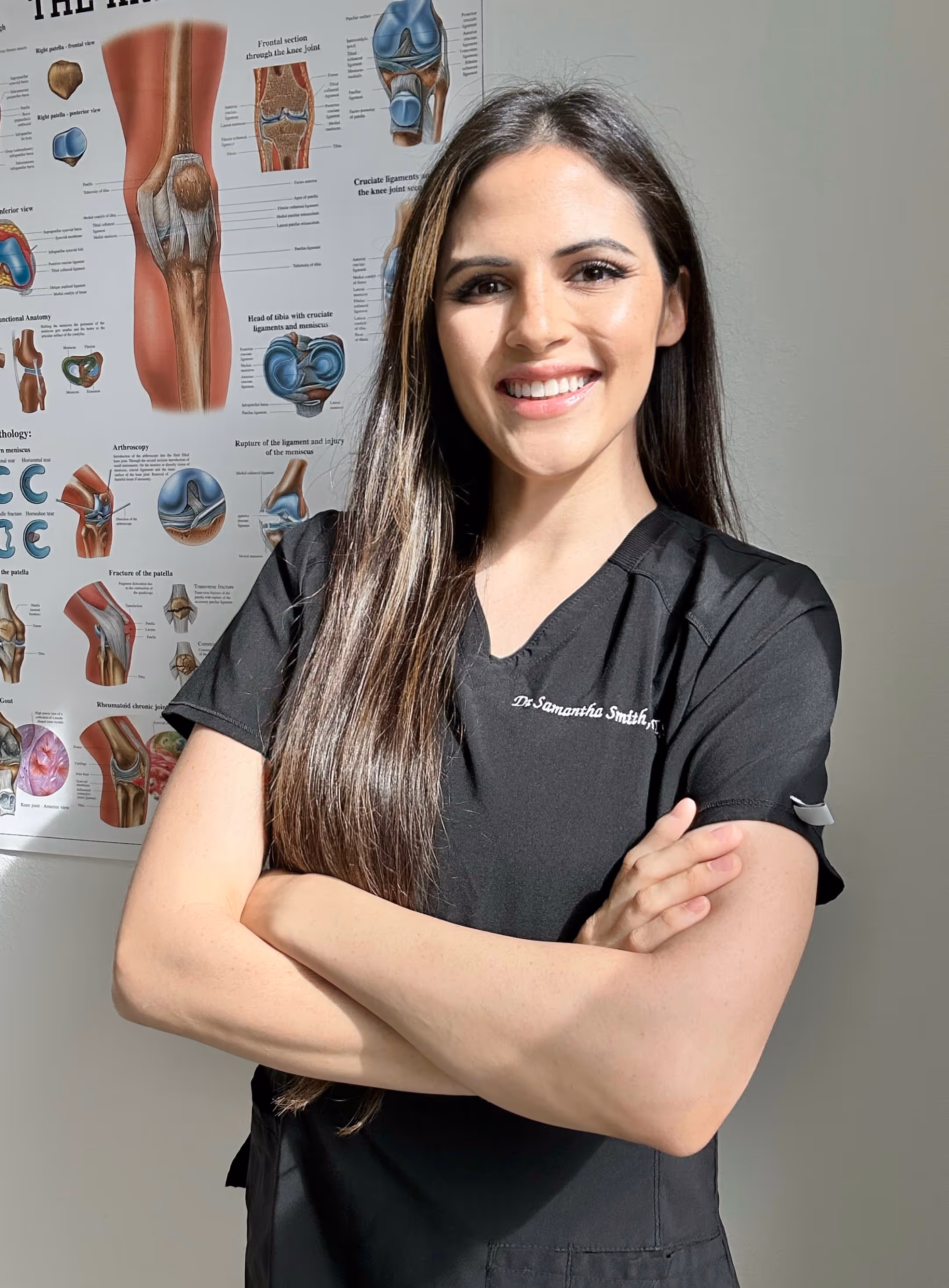 Smiling medical professional in black scrubs with knee anatomy posters behind