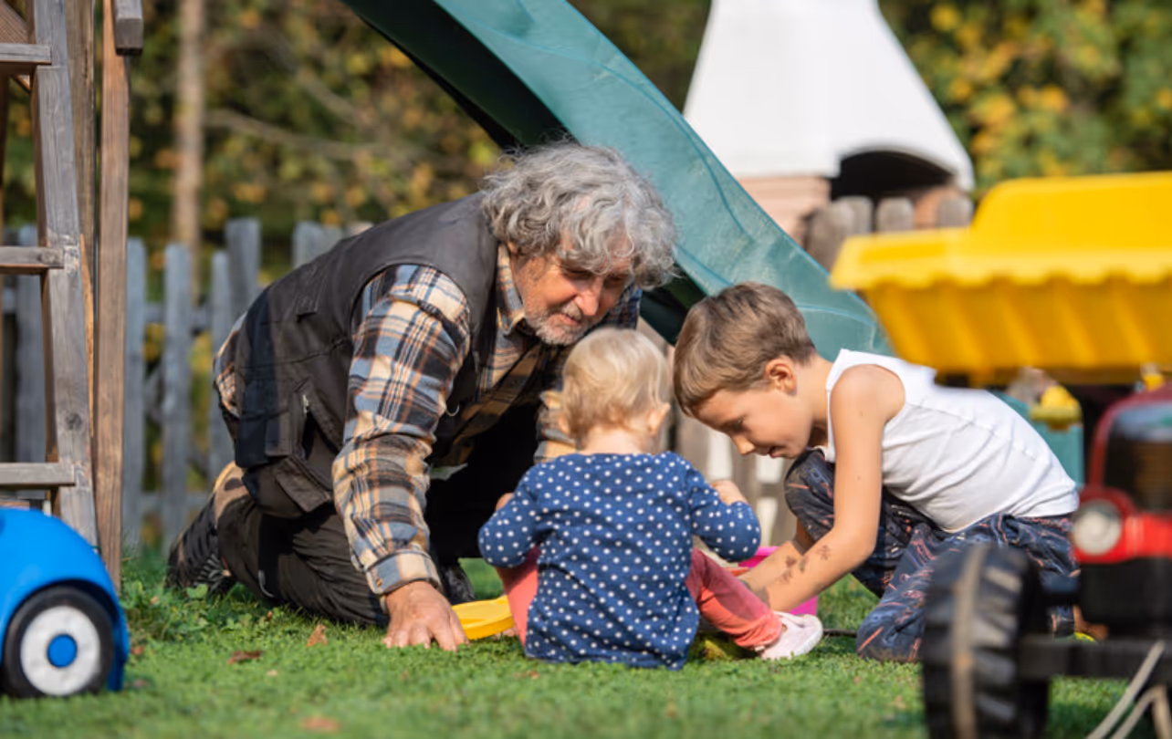 Grandfather playing with grandchildren on grass near playground slide