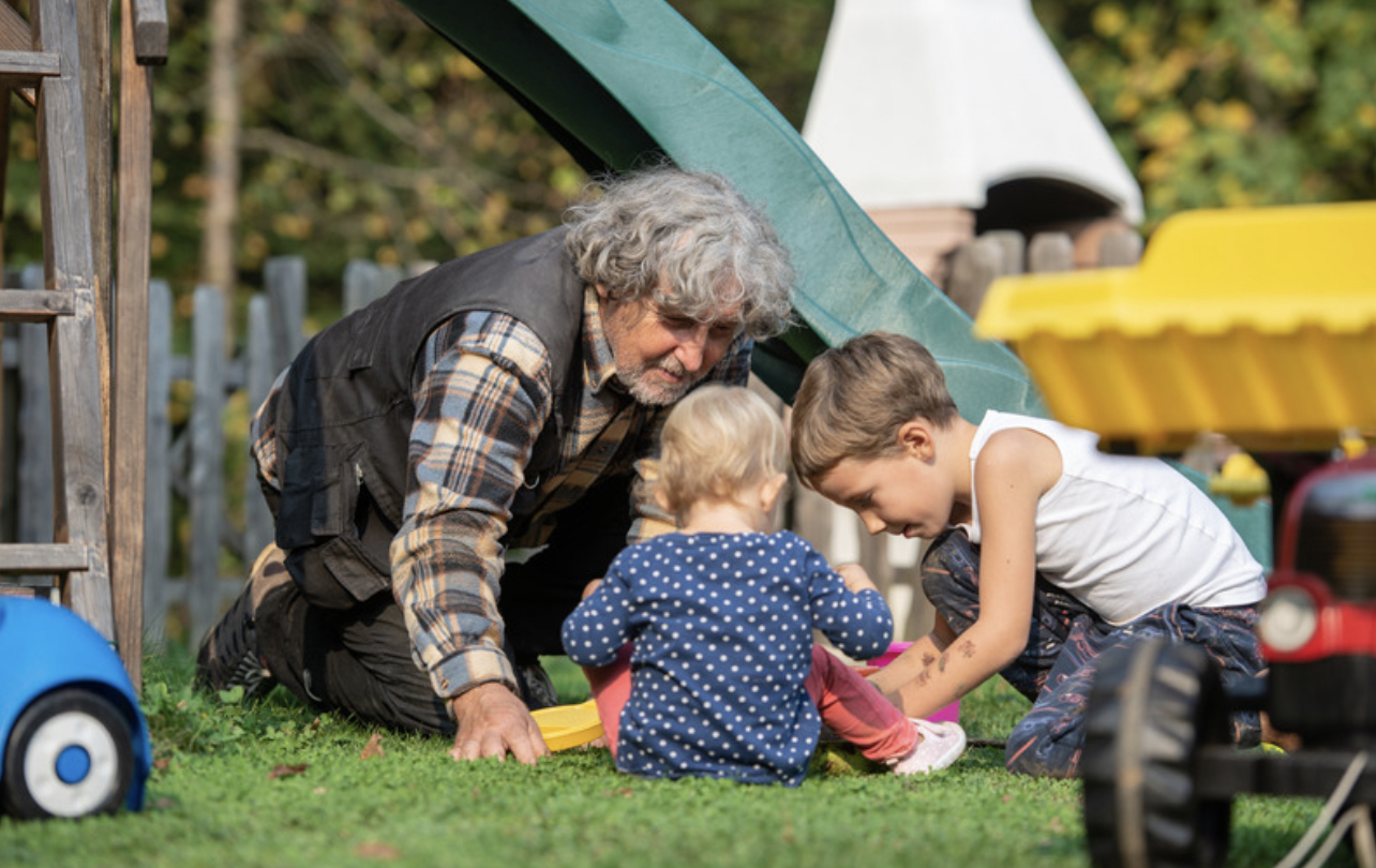 Grandfather playing with grandchildren on grass near playground slide