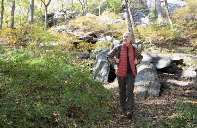 Hiker with backpack walking through rocky forest trail in autumn