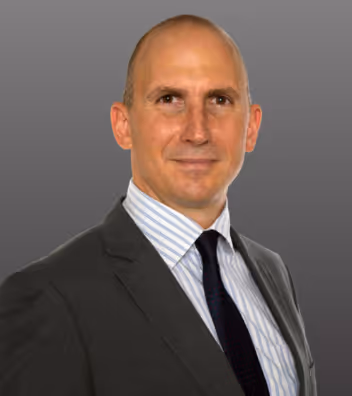 Középkorú férfi öltönyben és nyakkendőben szürke háttér előtt.