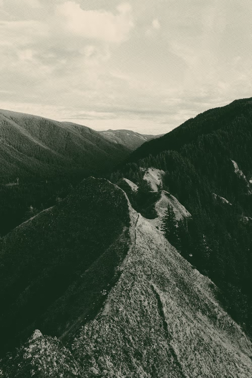 Textured photo of a mountain ridge trail surrounded by forested valleys and distant peaks under a cloudy sky