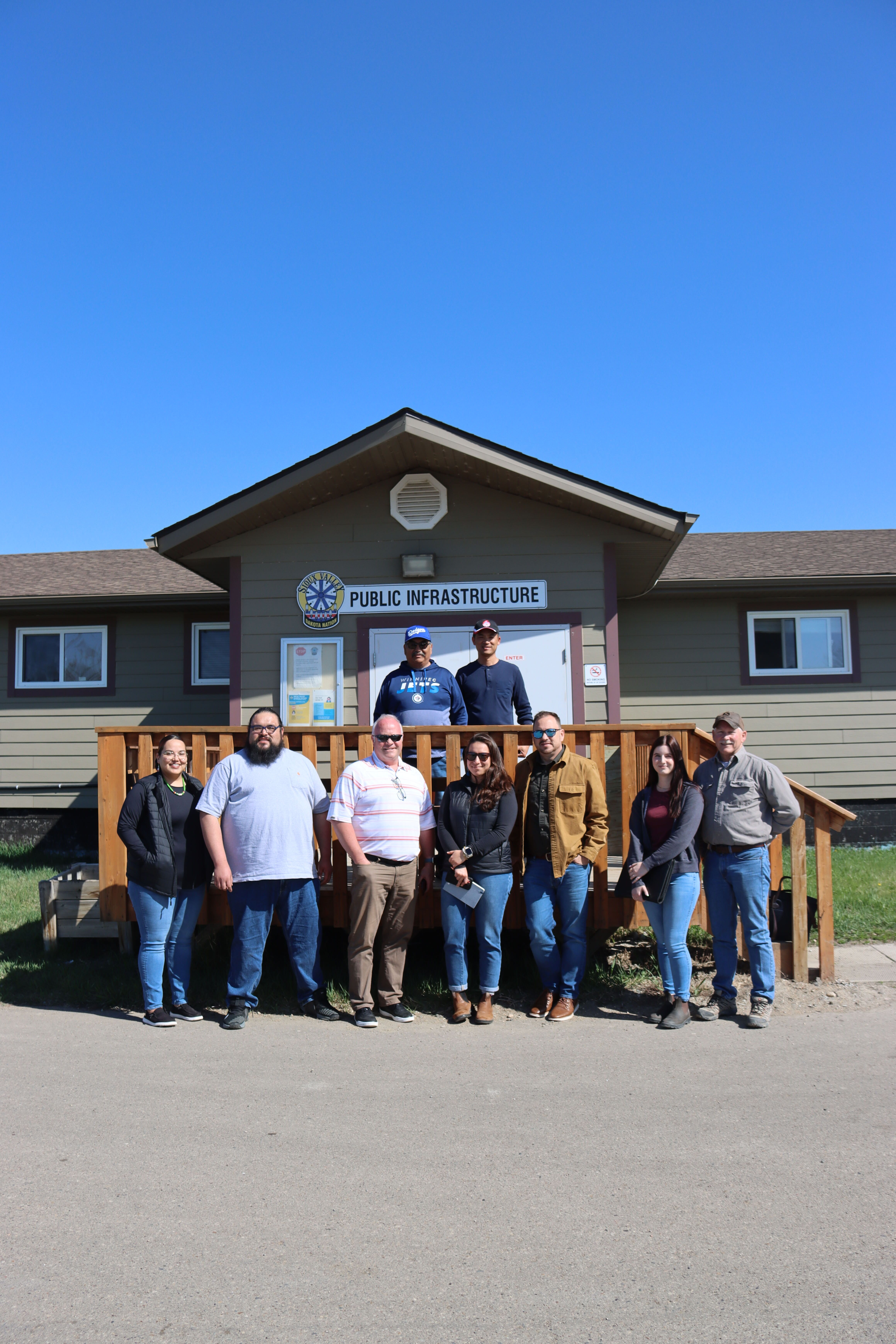 Raven Outcomes team and community members stand in front of Public Infrastructure office. 