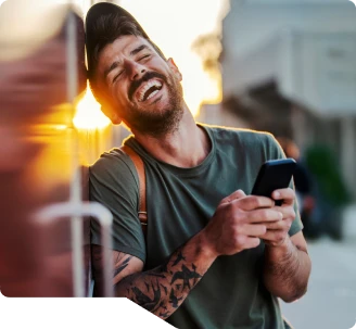 Foto de um rapaz de boné e roupa casual, rindo muito e feliz ao olhar seus resultados na tela de seu celular.