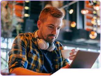 Foto de um rapaz, tomando seu café tranquilamente e verificando sua renda variável na tela de um tablet.