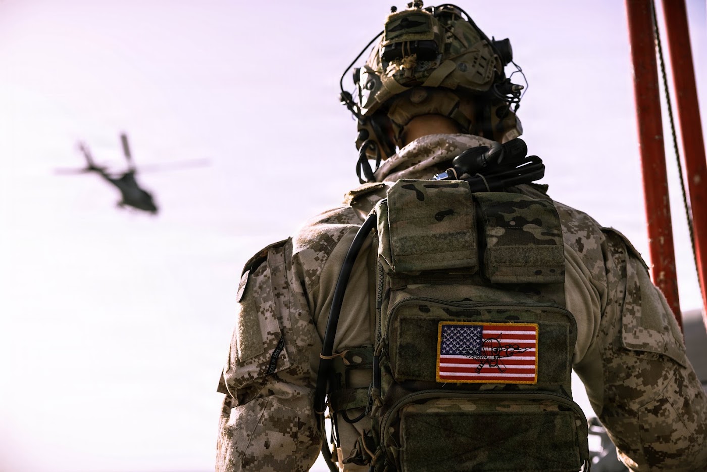 Service member seen from behind with an American flag patch, helicopter in the distance