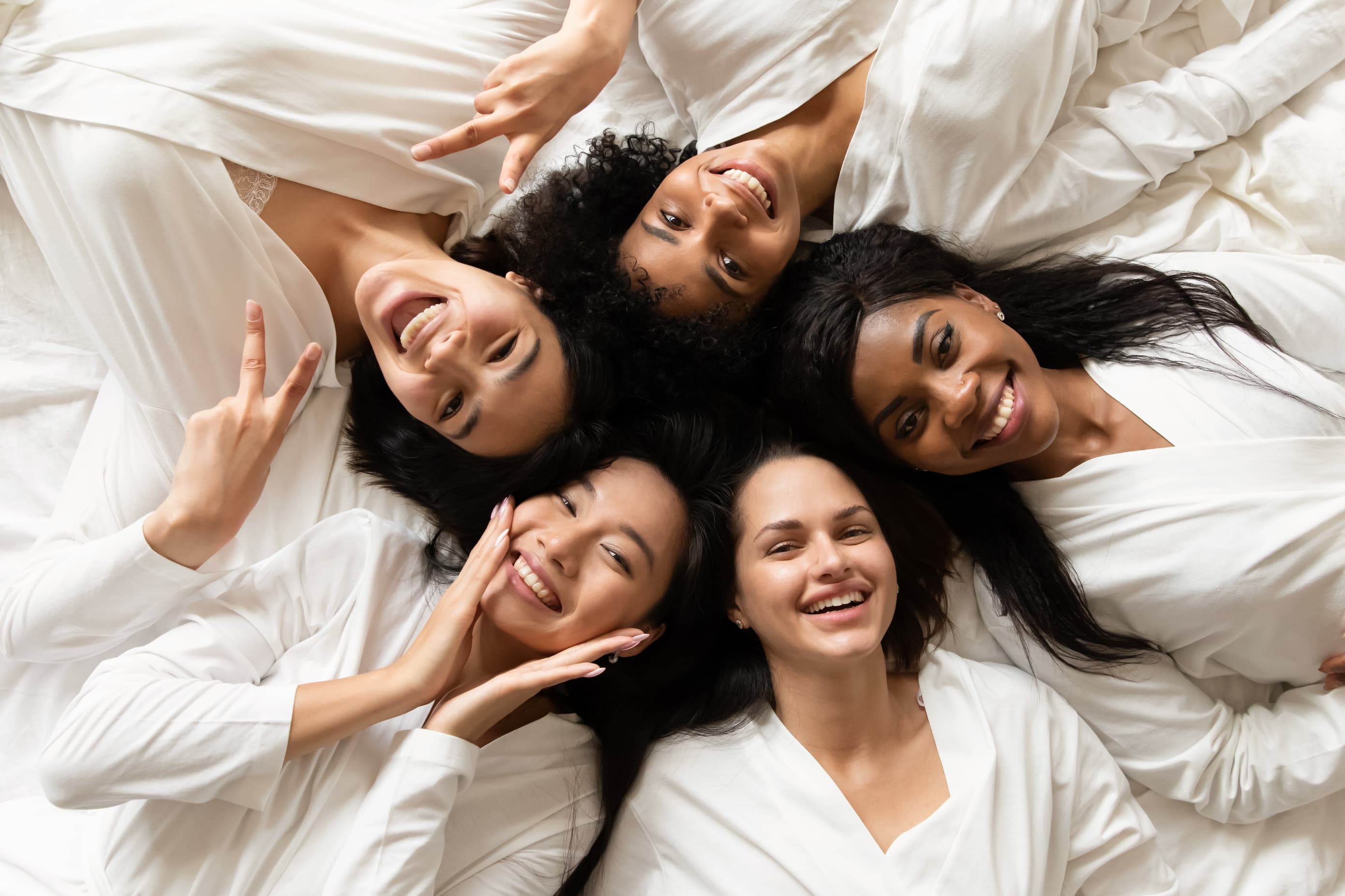 A group of women laying in a circle on a bed.