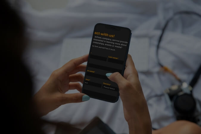 Person holding a smartphone displaying a contact form with fields for last name, phone number, email, and country selection.