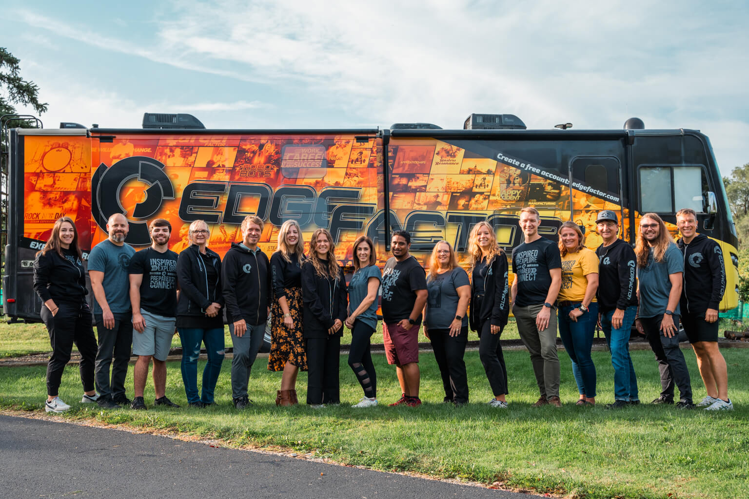 Group of 15 diverse people standing on grass in front of a bus with bright orange Edge Factor branding.
