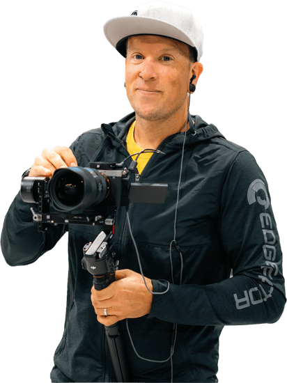 Jimmy Bender wearing a white cap and black Edge Factor jacket holding a professional camera mounted on a gimbal camera stabilizer.