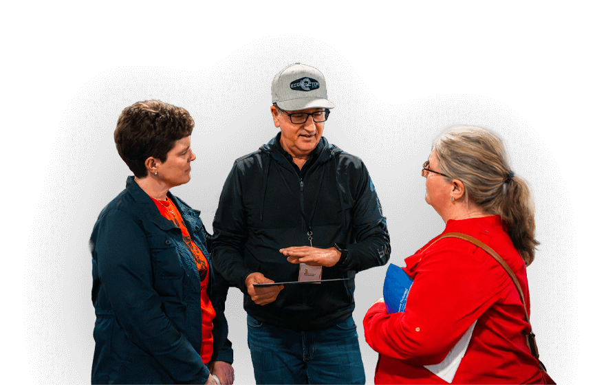 Three adults engaged in conversation, Carmine Romano wearing a gray cap and black Edge Factor jacket holds a clipboard, two female educators listen attentively.