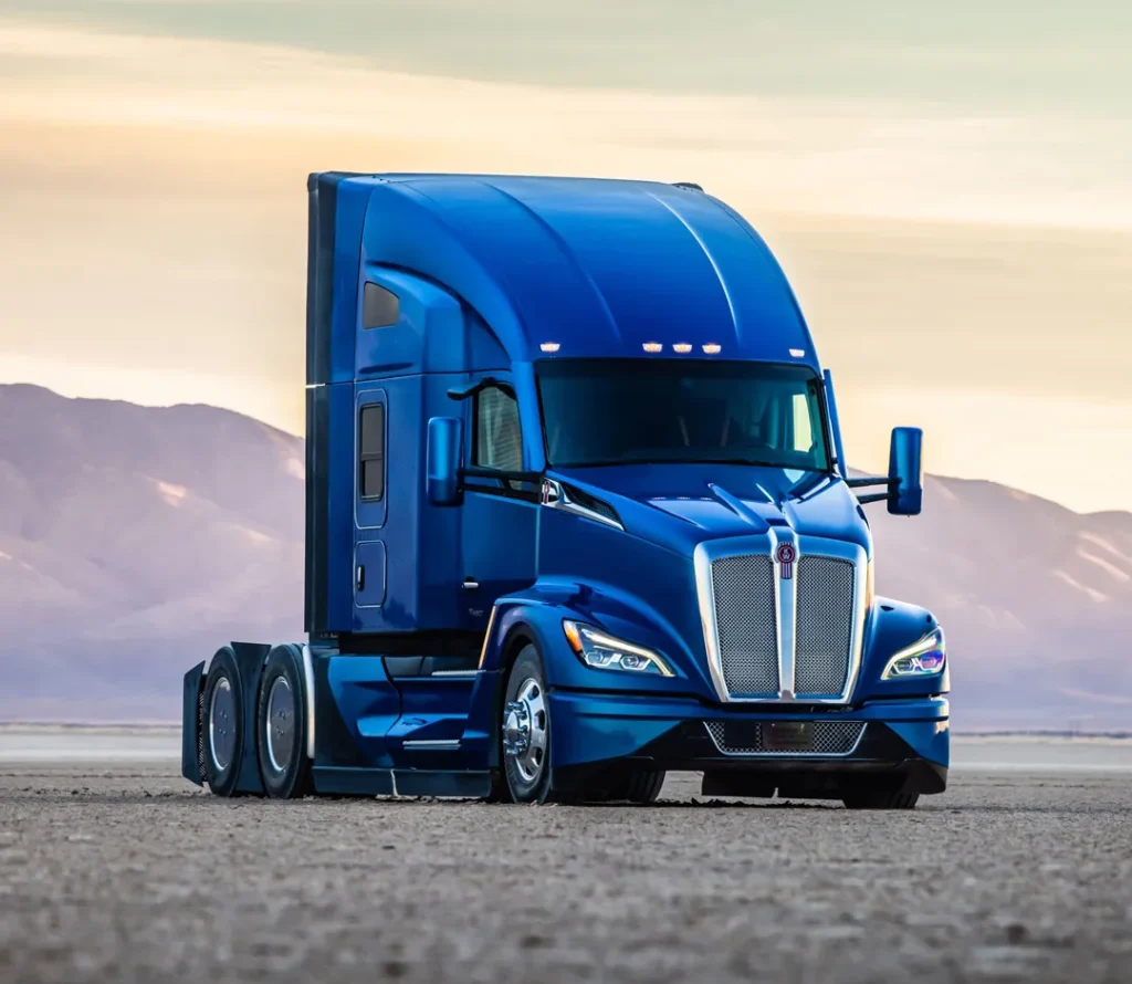 A blue Kenworth truck in gravel with mountains in the back.