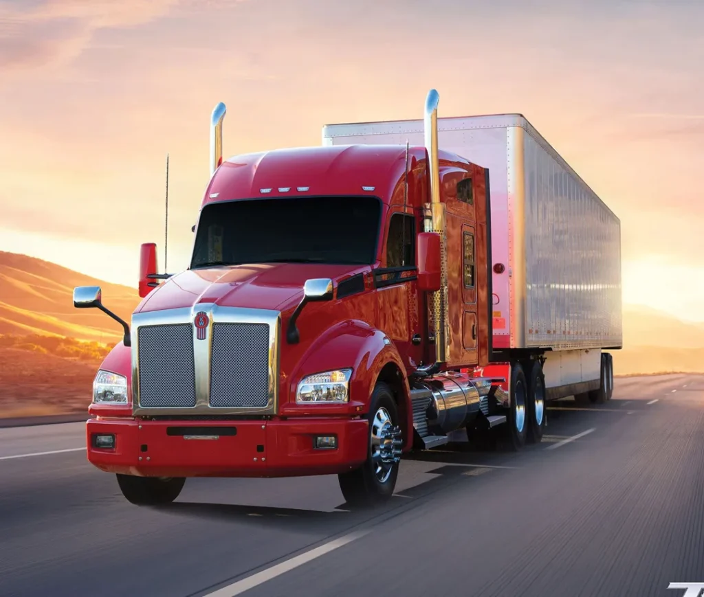 A red Kenworth T880 traveling in a road with a trailer attached, leaving the sun in the back.
