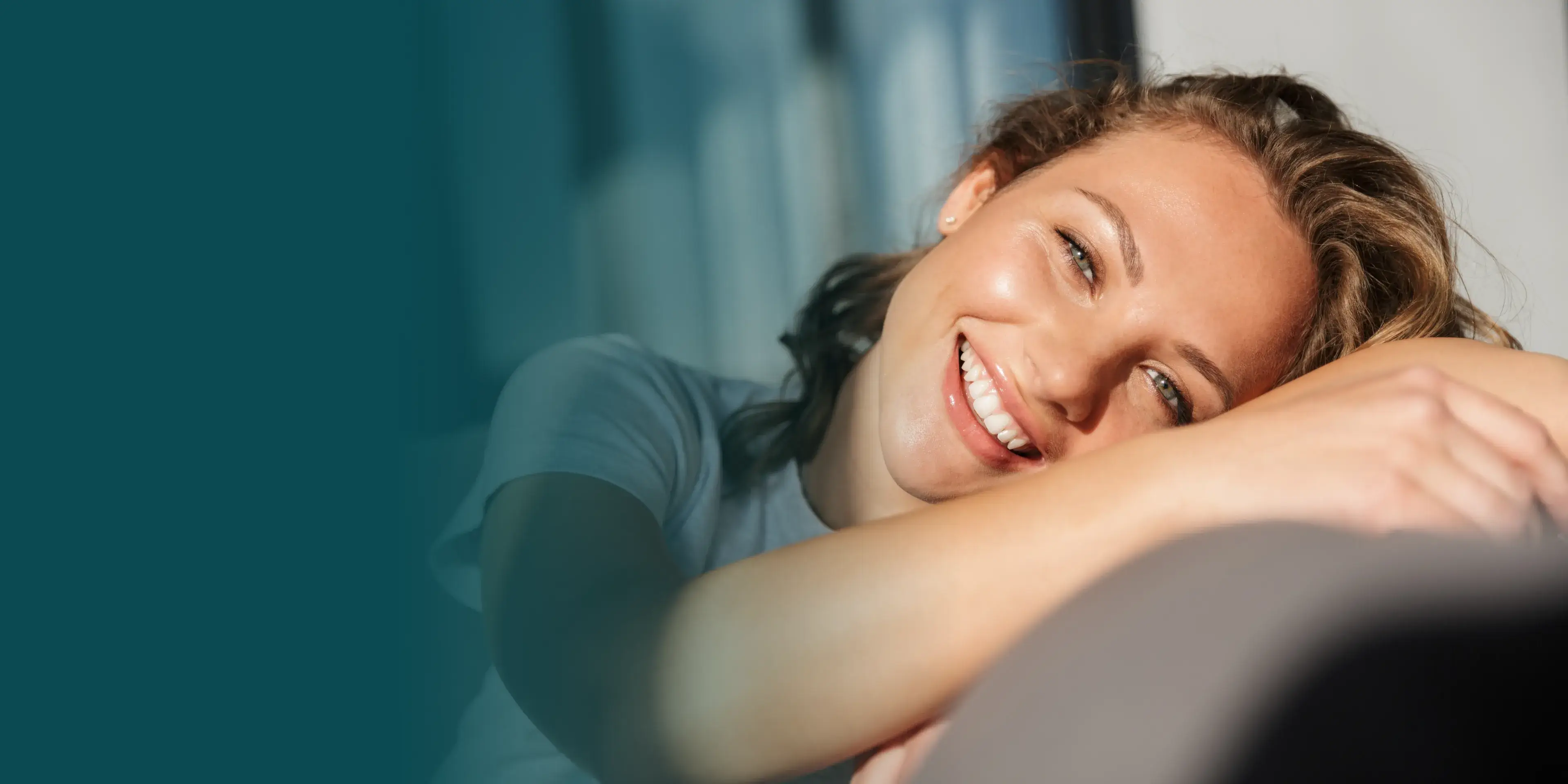 A woman smiling while resting her head on her arms.