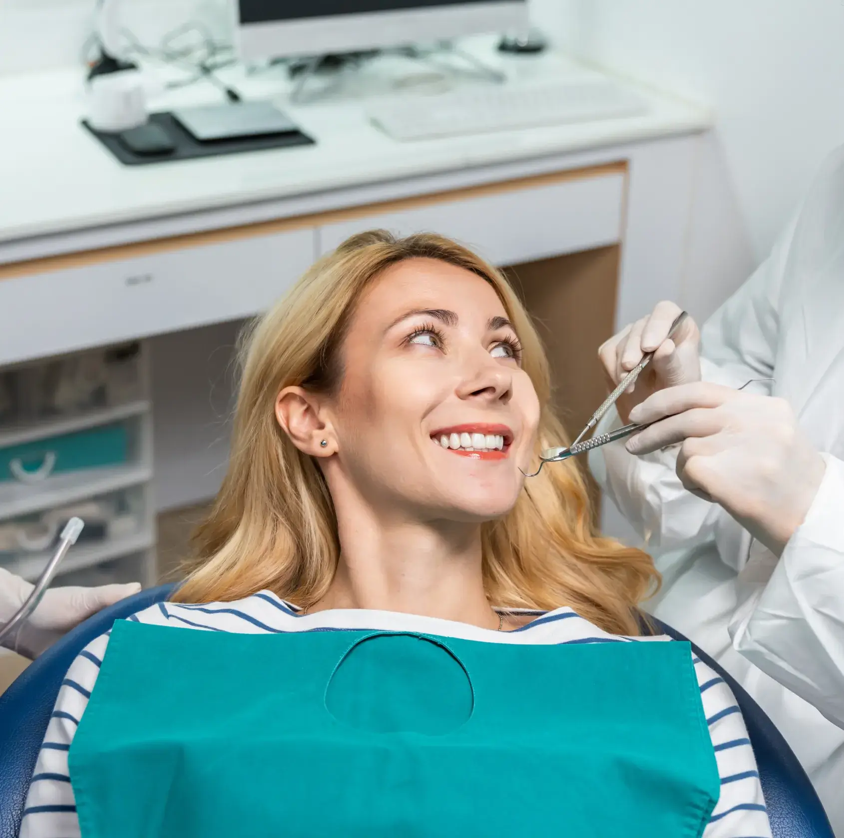 Woman sitting in a dental chair, smiling at the camera, with a dentist standing nearby.