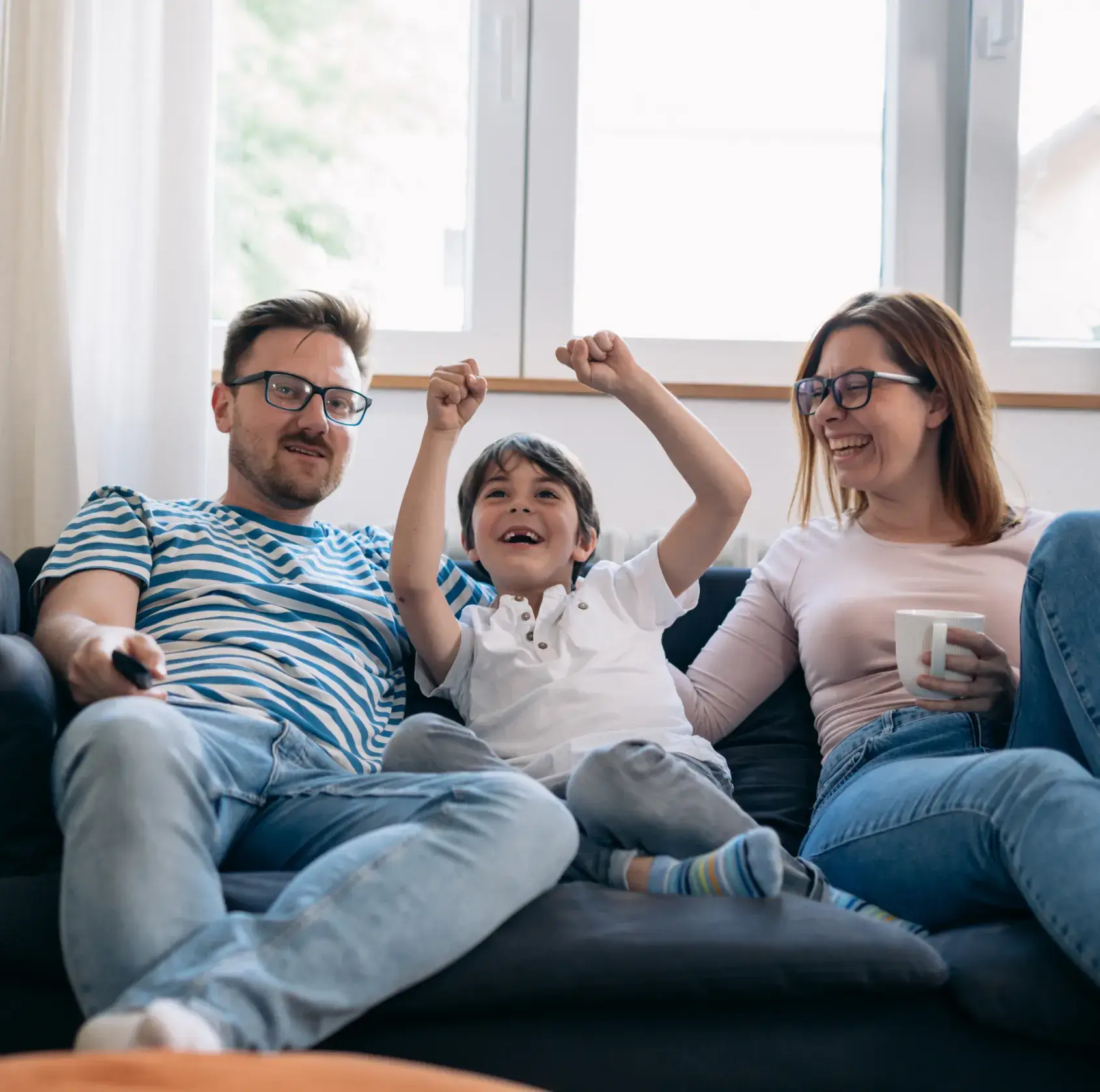 A family of three sits on a couch, smiling and celebrating together.