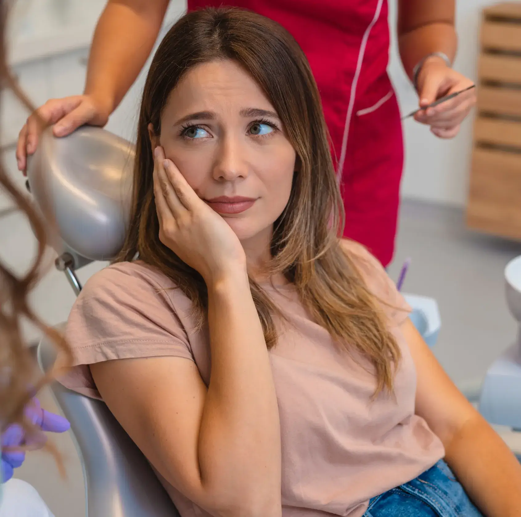 Woman sitting in a dental chair, holding her cheek with a concerned expression.
