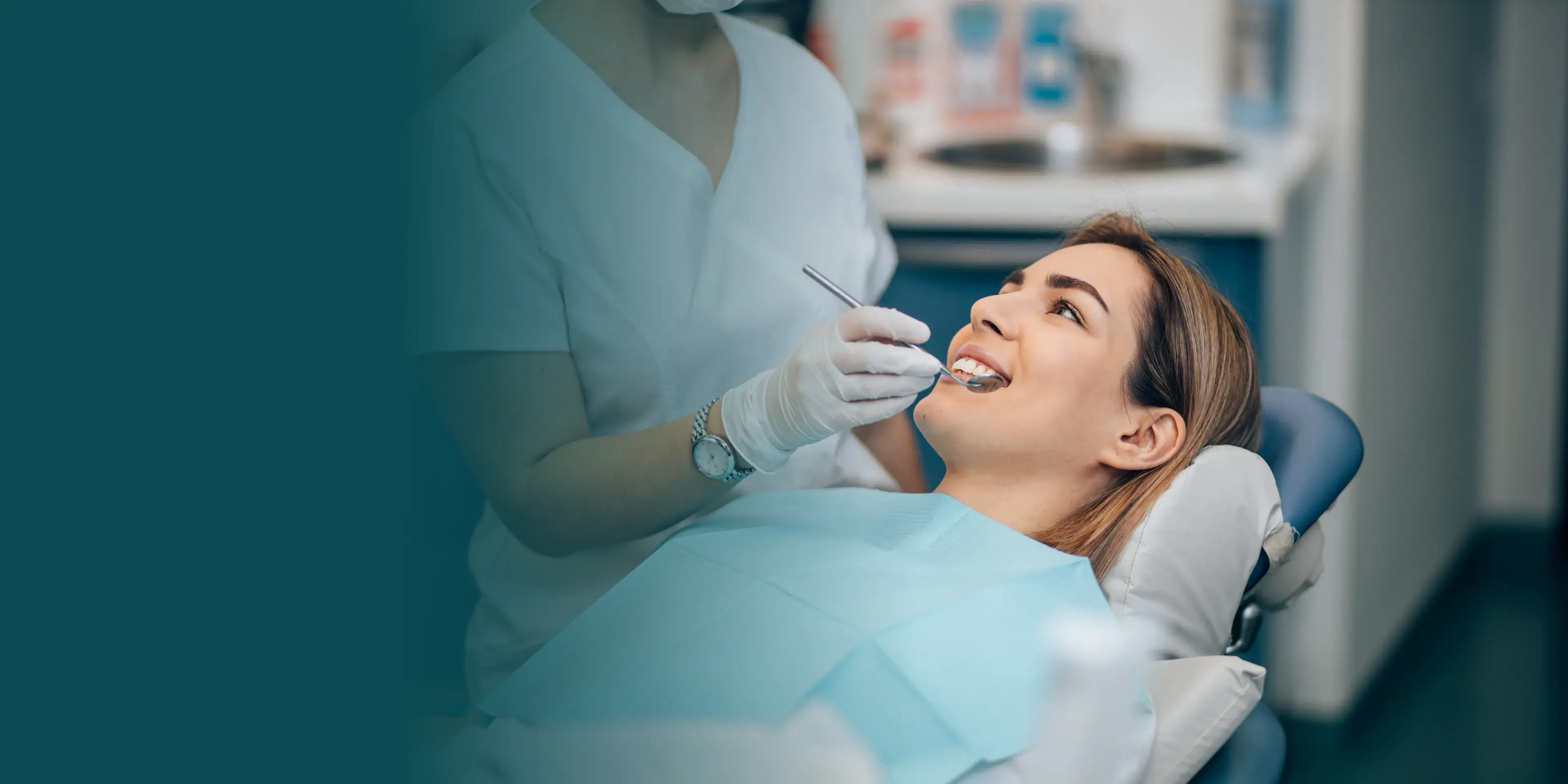 A woman is sitting in a dental chair, smiling at the dentist who is holding dental tools.