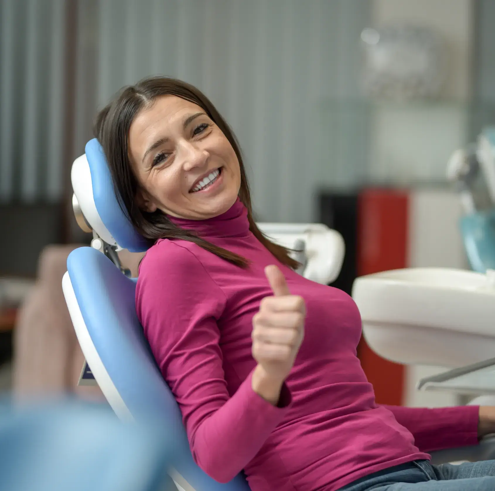 A woman in a dental chair smiles and gives a thumbs up.