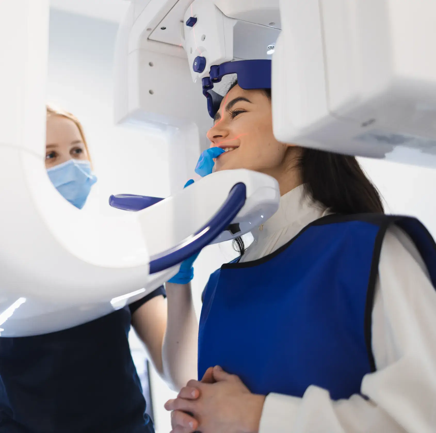 A person smiles in a mirror while a dentist shows them two clear dental aligners.