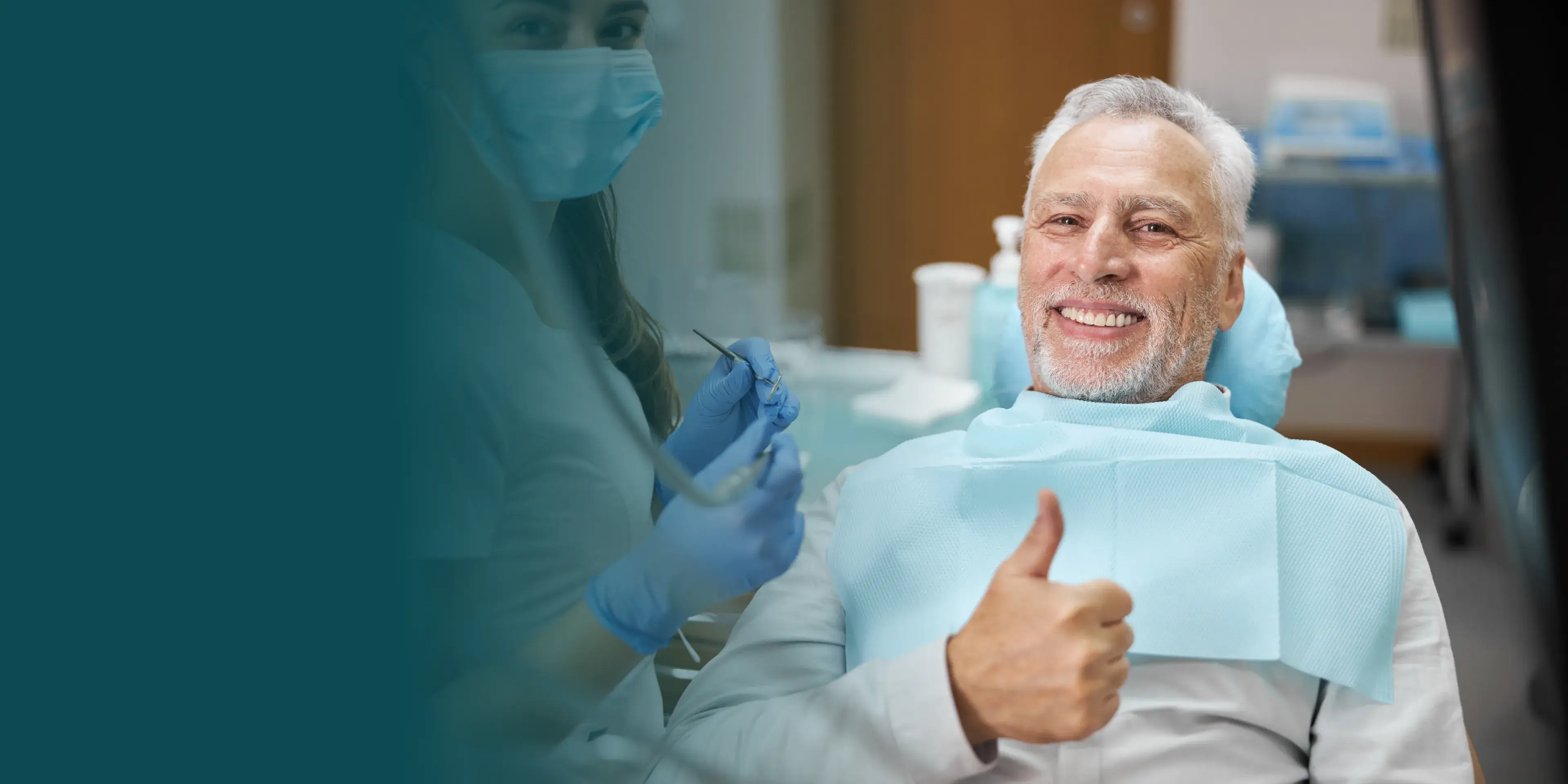 A man sitting in a dental chair gives a thumbs up, next to a dental professional.