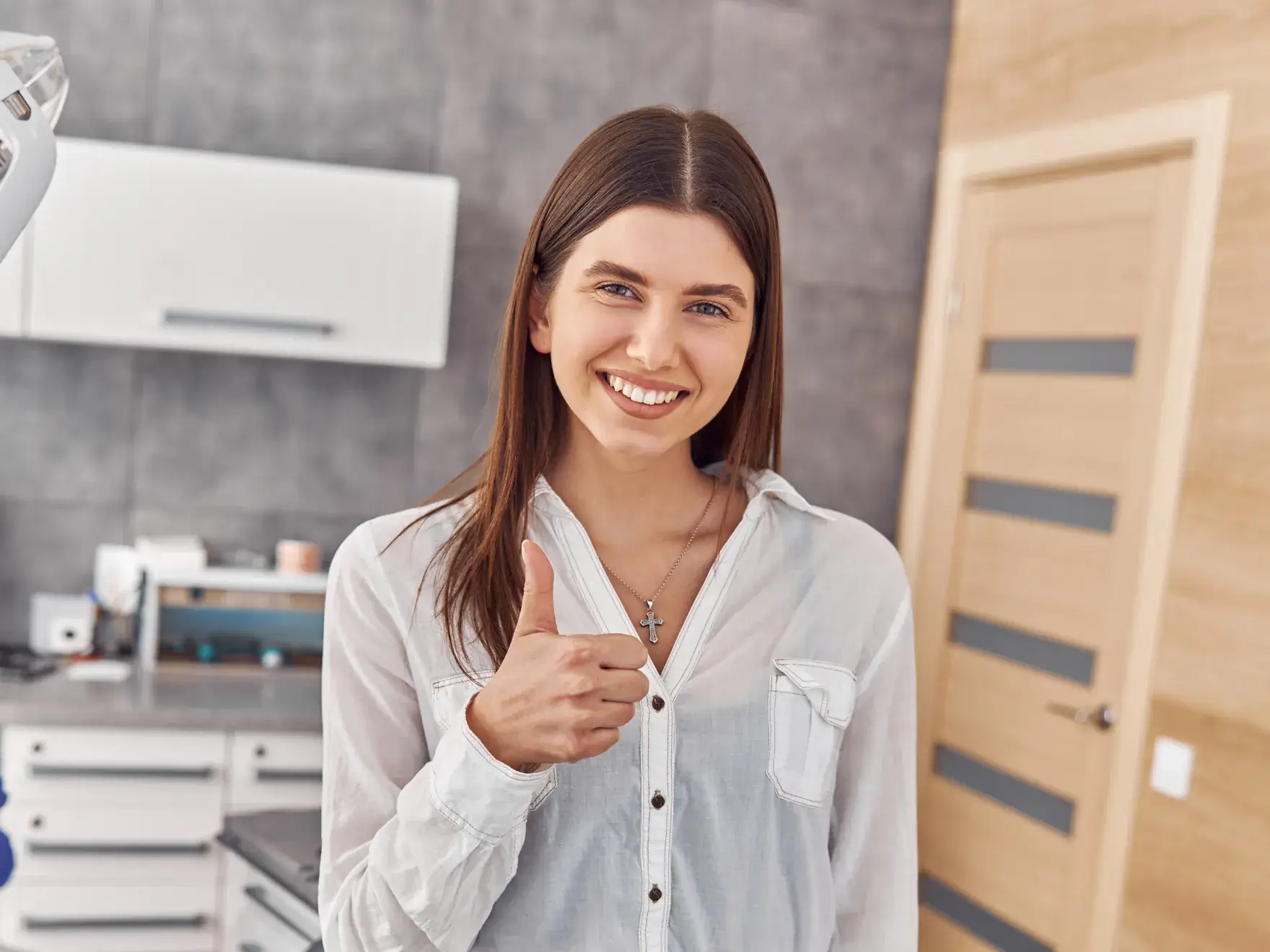 A woman in a white shirt gives a thumbs-up in a modern kitchen.