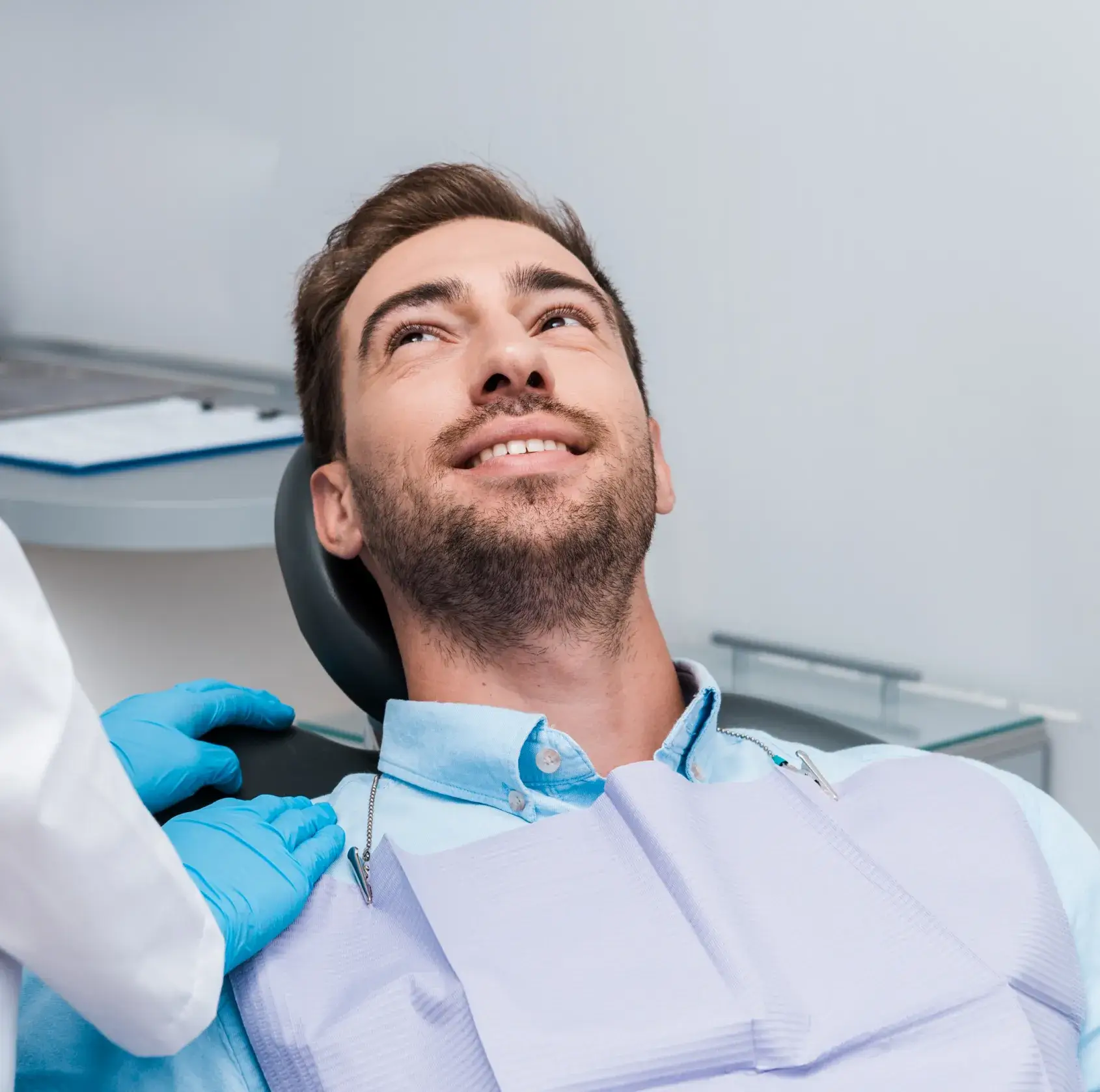 A man is sitting in a dental chair, smiling, with a dentist's hand on his shoulder.