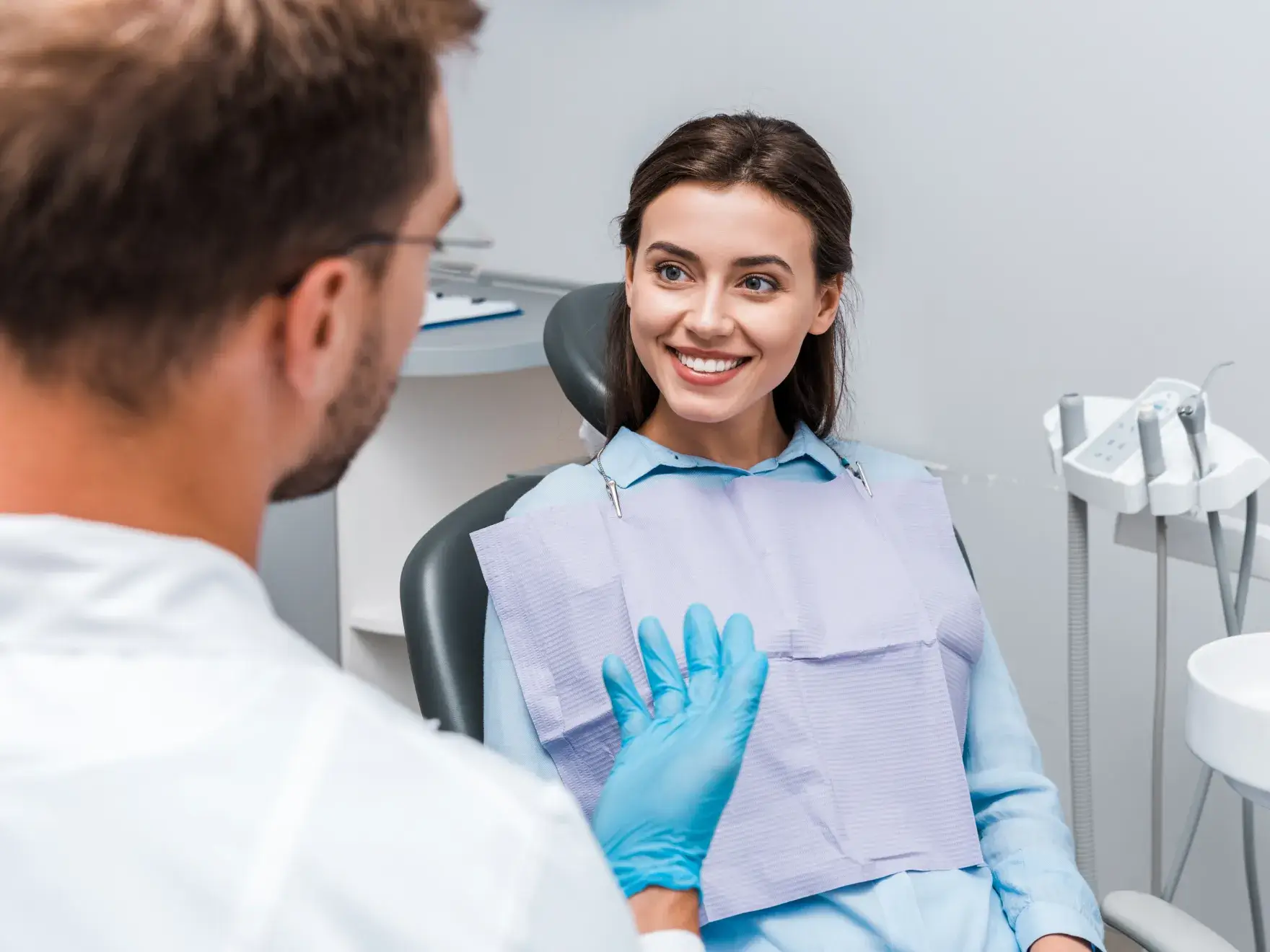 A dentist examines a smiling patient in a dental chair, holding a dental instrument.