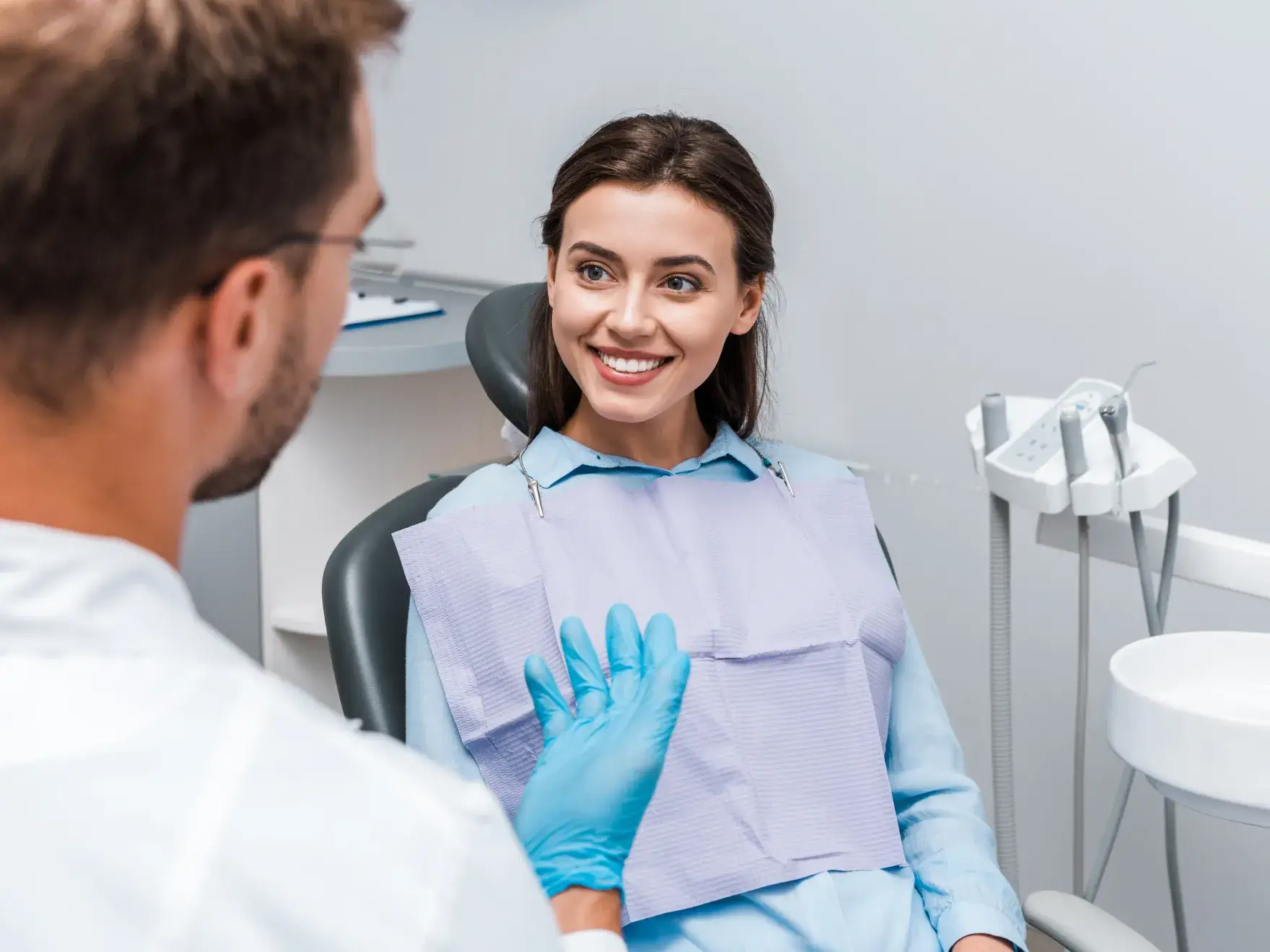 Smiling woman holding a clear dental aligner, taking a selfie against a neutral background.