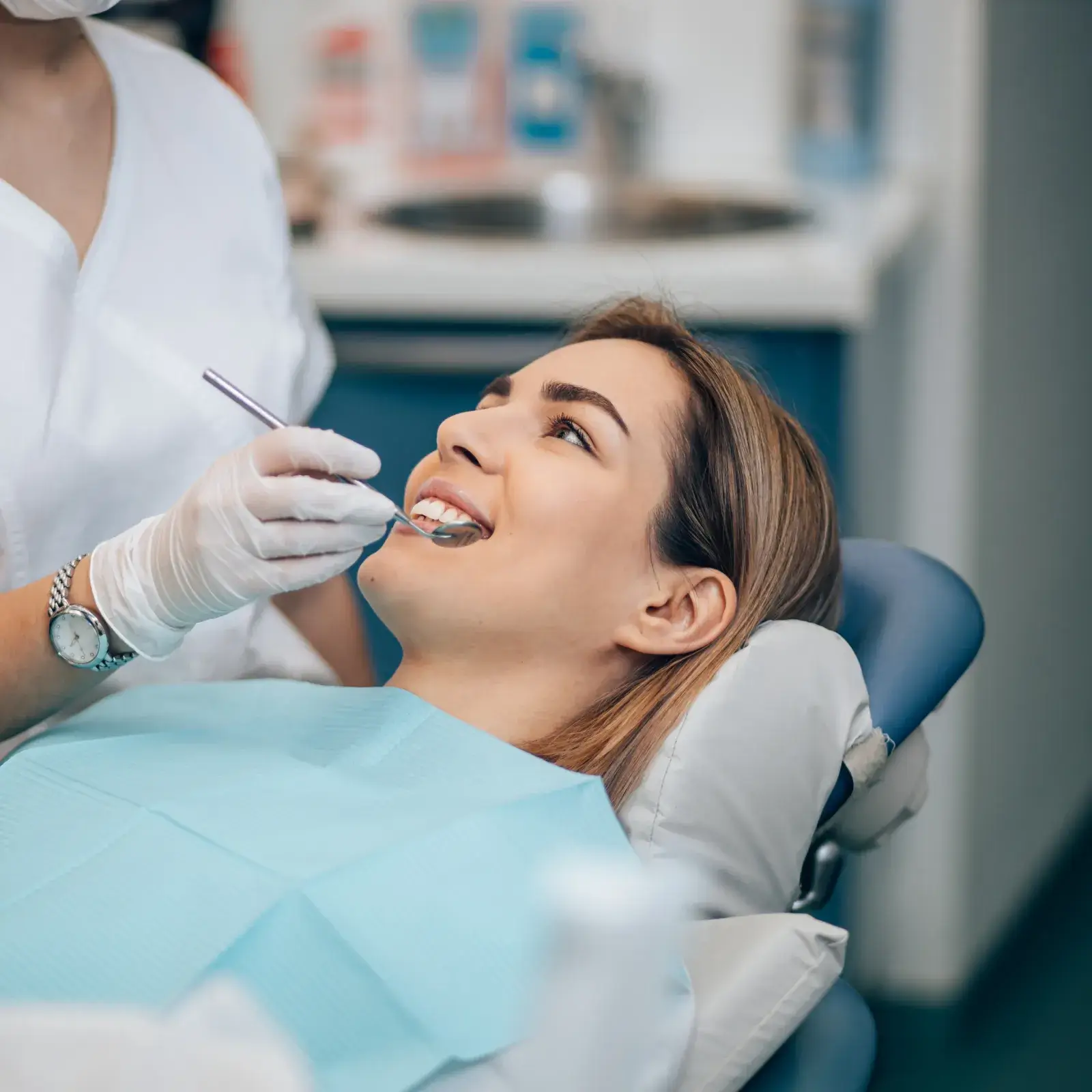 A dentist examines a smiling woman's teeth using a dental tool in an office.